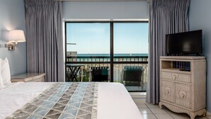 Habitación de hotel con una cama grande, un televisor en un mueble y un balcón con vista al mar.
