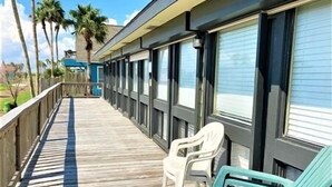 A wooden deck with a railing, a row of windows, and a few plastic chairs. - Three Bedroom, Two Bath. Off Water Home. Short Distance to Public Pier. (Port Mansfield)