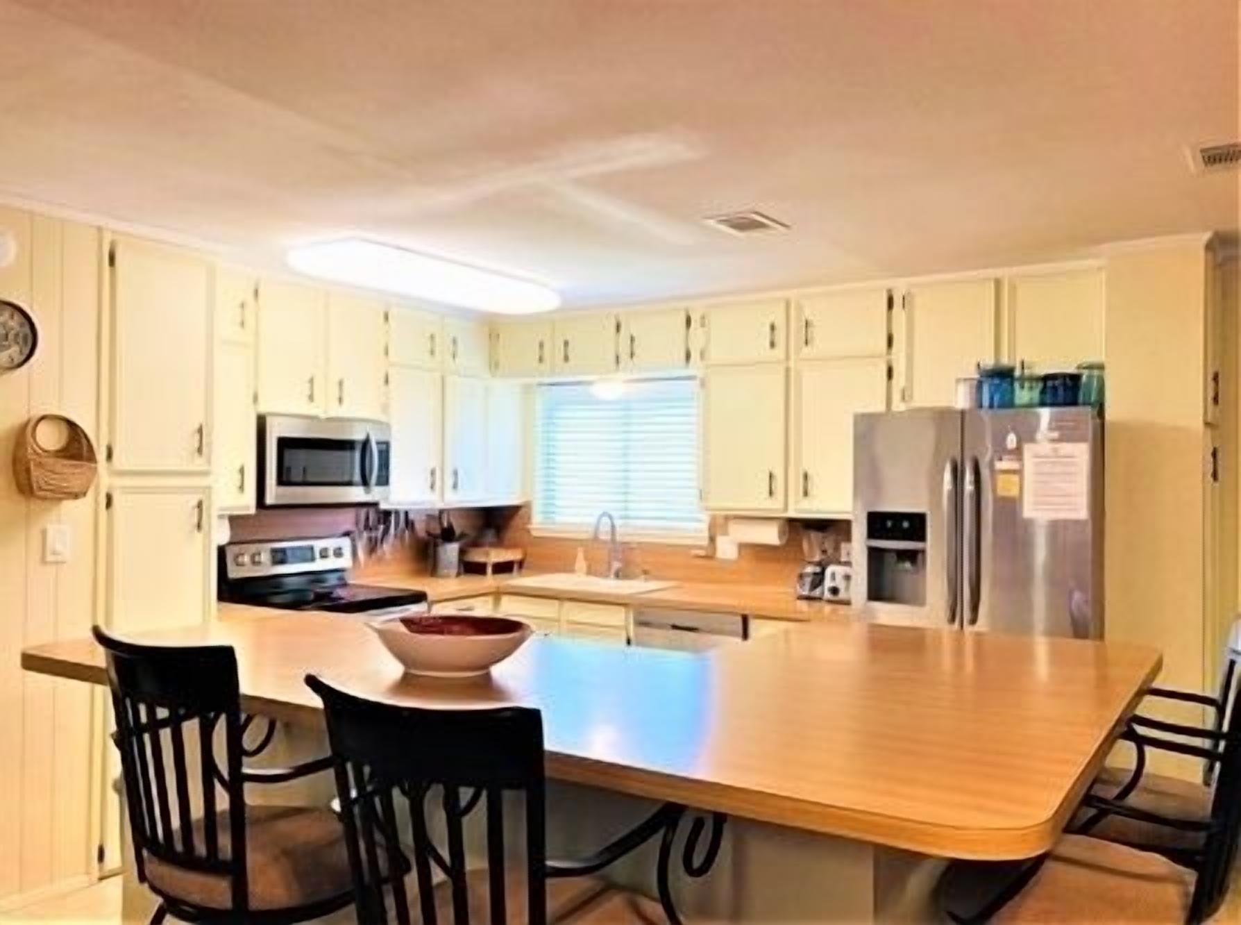 A compact kitchen with white cabinets, a microwave, a stove, a refrigerator, and a dining area with a wooden table and four chairs.