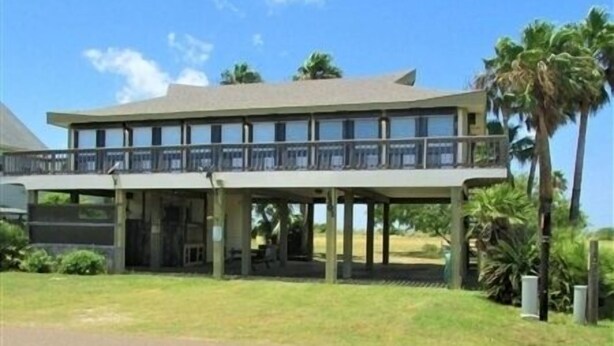 A two-story building with a balcony on the upper floor, surrounded by greenery and palm trees. - Three Bedroom, Two Bath. Off Water Home. Short Distance to Public Pier. (Port Mansfield)