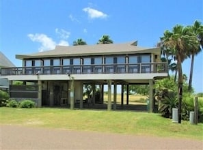 A two-story building with a balcony on the upper floor, surrounded by greenery and palm trees.