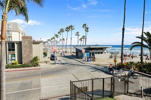 A beachfront street with palm trees, a beachside building, and a gated entrance.