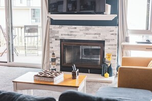 A living room with a fireplace, a sofa, a coffee table, and a view of the outside balcony.