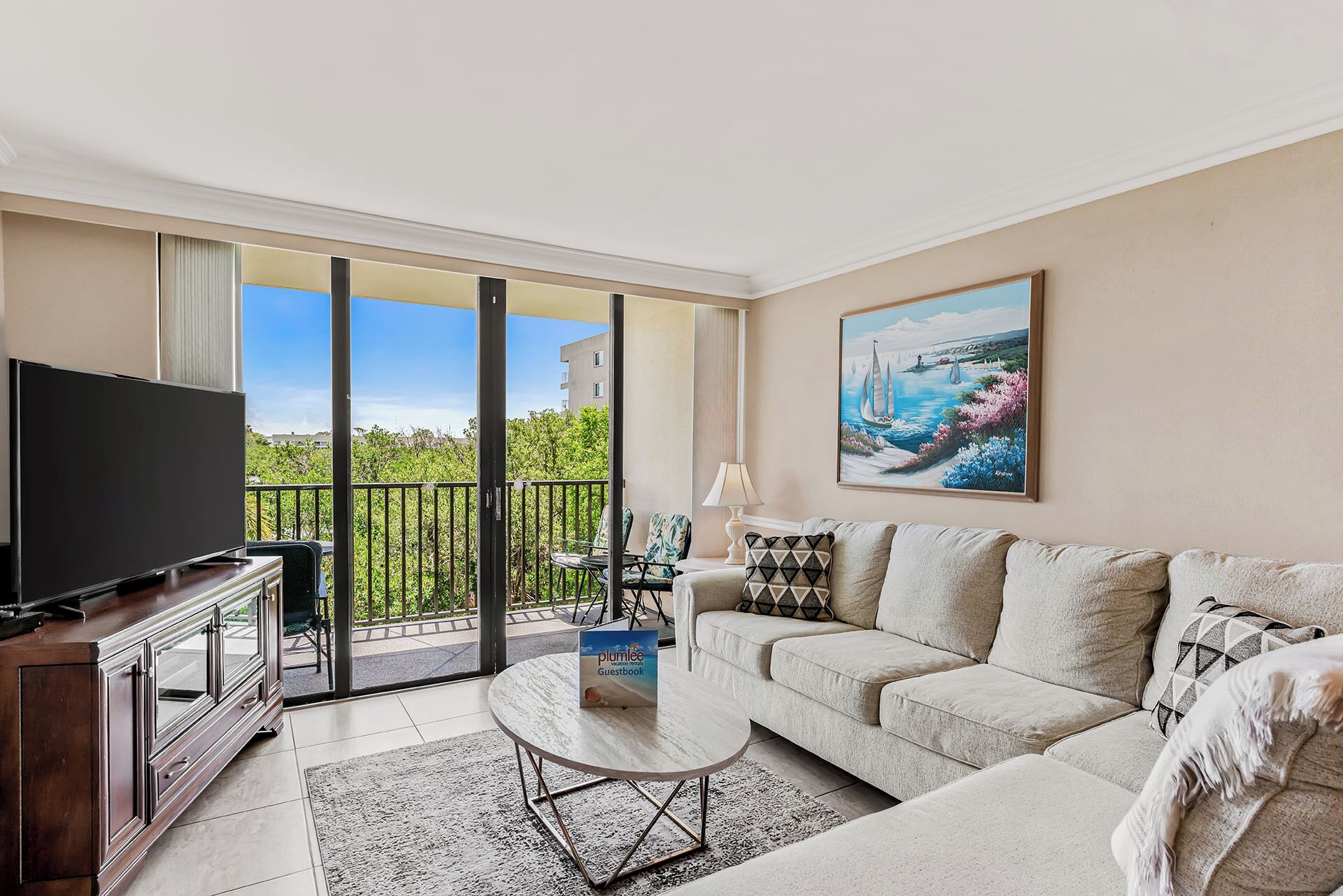A modern living room with a flat-screen TV, a sofa, a coffee table, and a painting of a coastal scene.