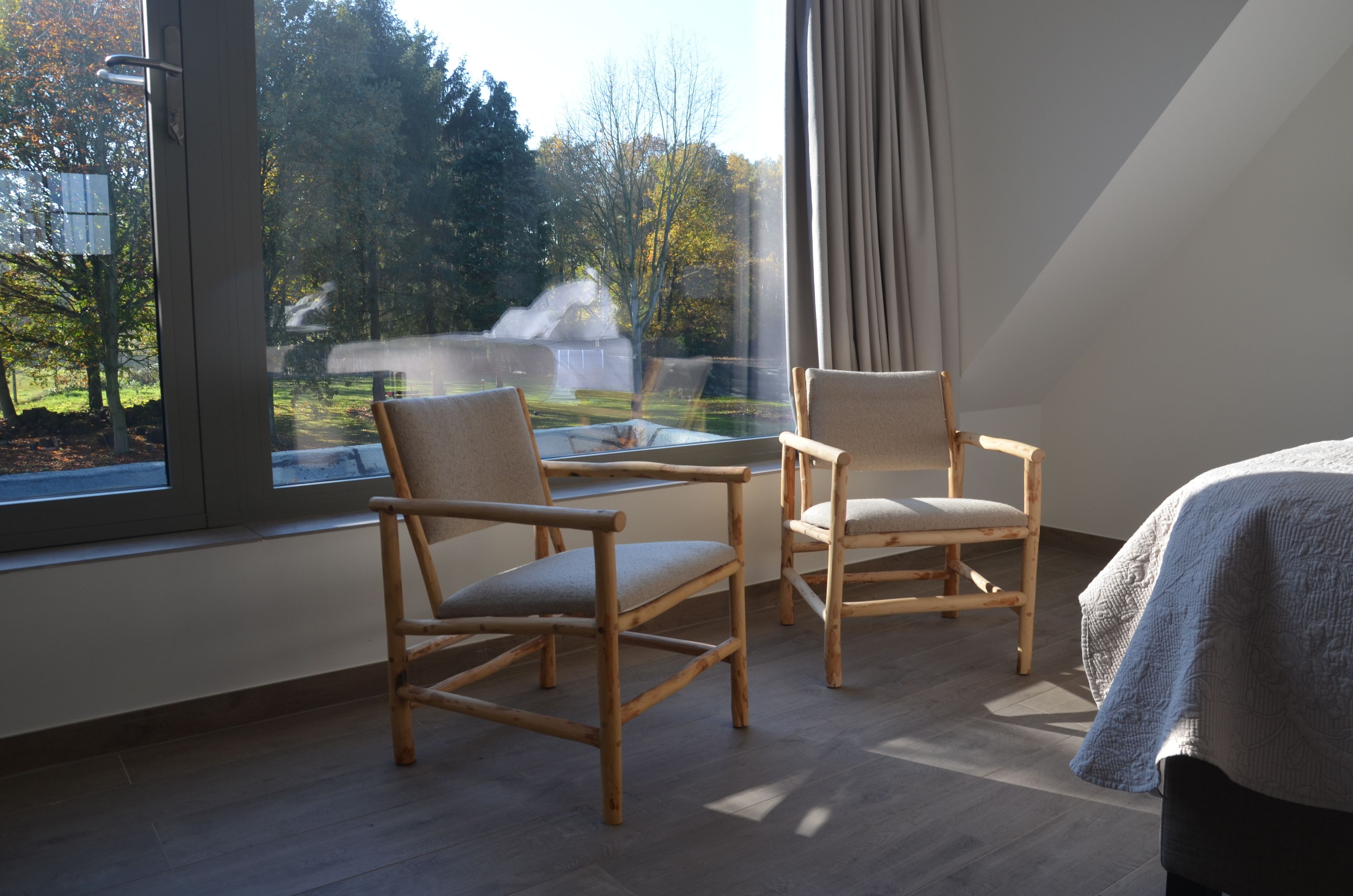 Een kamer met twee houten stoelen, een glazen tafel en een bed met dekbed.