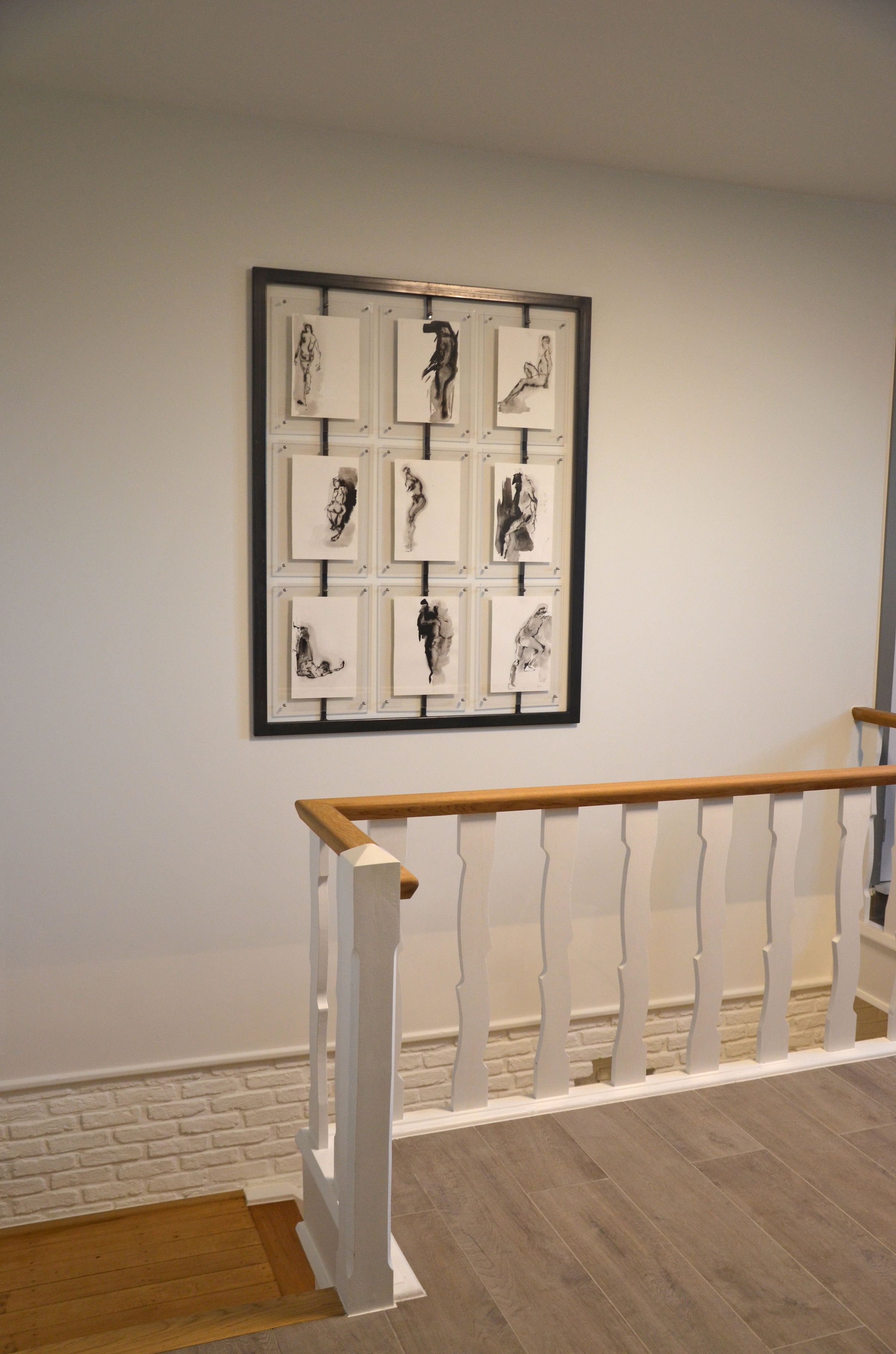 A staircase with a wooden handrail and white balusters, leading to a landing with a framed artwork of black and white sketches.