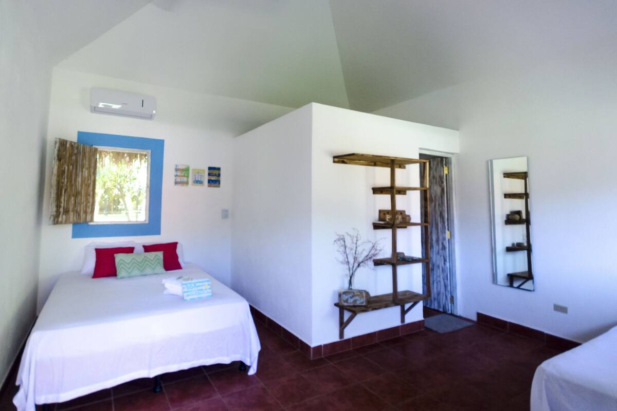 A bedroom with a bed, a window with curtains, a wall-mounted air conditioner, and a wooden shelf unit.