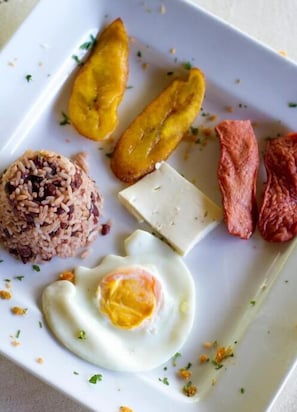A plate with rice, fried plantains, a piece of meat, a fried egg, and a slice of cheese. - Las Dunas Surf Resort - Hostel (El Viejo)