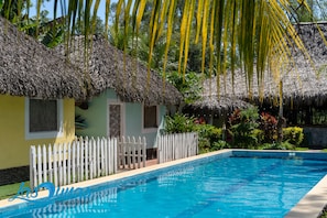 A pool area with a thatched-roof hut, white picket fence, and lush tropical vegetation. - Las Dunas Surf Resort - Hostel (El Viejo)