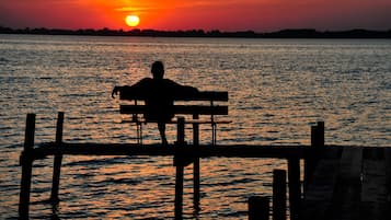 A silhouette of a person sitting on a bench at sunset by a body of water.