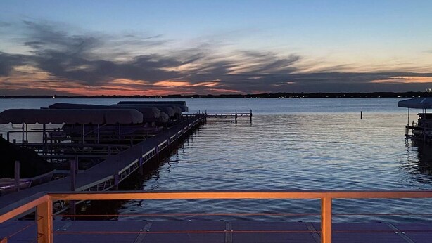 A waterfront deck with a fire feature, overlooking calm water and a sunset sky. - Lakeside Inn (Clear Lake)