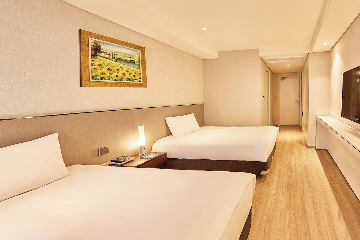 A hotel room with two beds, a painting on the wall, and a TV on the right.