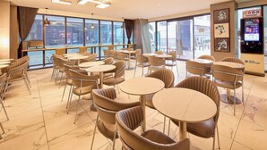 A modern cafe with round tables and cushioned chairs, large windows, and a money exchange machine. - Hotel Thomas Myeongdong (Seoul)