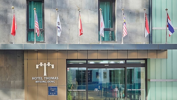 A hotel facade with multiple windows, flags, and a sign reading "HOTEL THOMAS MYEONG DONG". - Hotel Thomas Myeongdong (Seoul)
