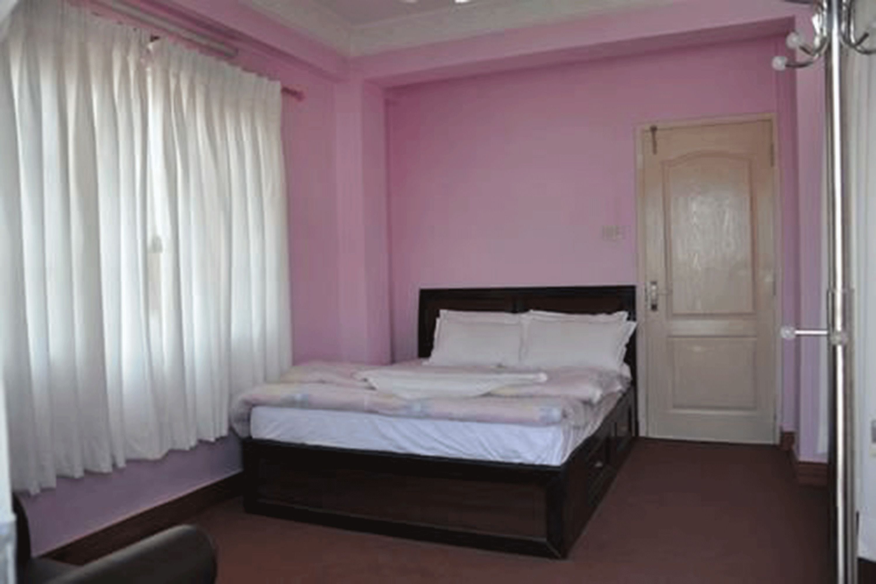 Un dormitorio con una cama individual, una puerta y una ventana con cortinas.