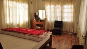 A bedroom with a bed, a desk, a chair, and curtains. - Bliss Apartment (Kathmandu)