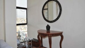 A room with a large window, a round mirror, and a small wooden table with a decorative item on it. - Bliss Apartment (Kathmandu)