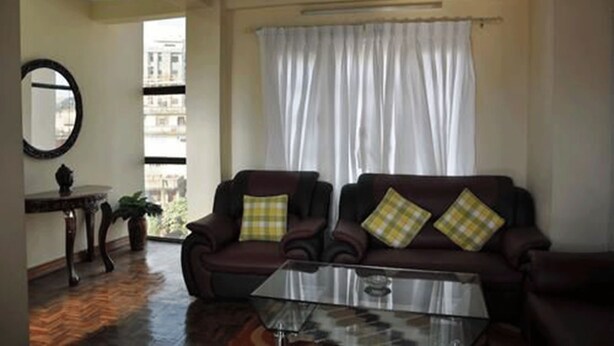 A living room with a sofa set, a glass coffee table, a round mirror, and a view of the outside. - Bliss Apartment (Kathmandu)