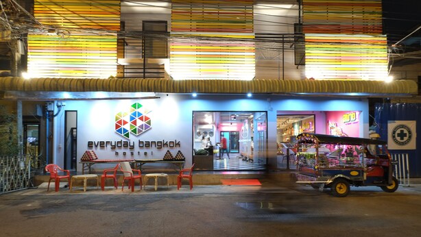 Une devanture de magasin bien éclairée, avec un auvent coloré et une enseigne sur laquelle on peut lire « Bangkok, jour après jour ».