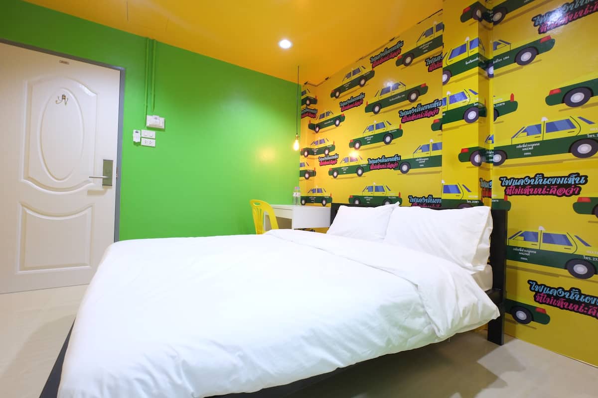 Une chambre à coucher avec un lit, une porte blanche et un mur orné d’un motif représentant des voitures jaunes et vertes.