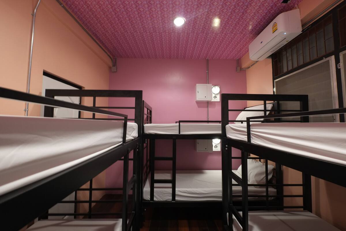 Une chambre avec quatre lits superposés, des murs roses, un ventilateur de plafond et un appareil de climatisation.