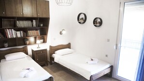 A room with two single beds, a wooden wardrobe, a small desk with a lamp, and a sliding glass door to the outside. - Villa Jasmine (Agios Vasileios)