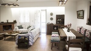 A cozy living room with a fireplace, a sofa, a dining table, and a bench. - Villa Jasmine (Agios Vasileios)