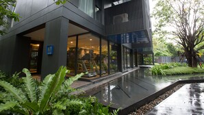 A modern building with large glass windows, a covered outdoor area, and a garden with a water feature. - The Deck Condo Patong by VIP (Patong)
