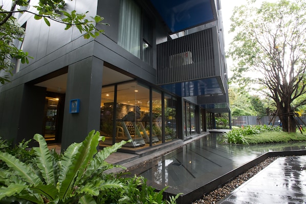 A modern building with large glass windows, a covered outdoor area, and a garden with a water feature.