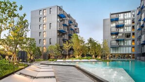 A modern building with balconies, a swimming pool, and a wooden deck. - The Deck Condo Patong by VIP (Patong)