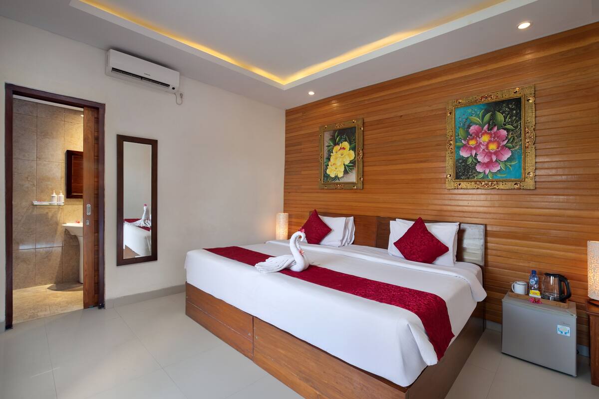 A hotel room with a large bed, wooden paneling, a small refrigerator, and a bathroom with a sink and mirror.