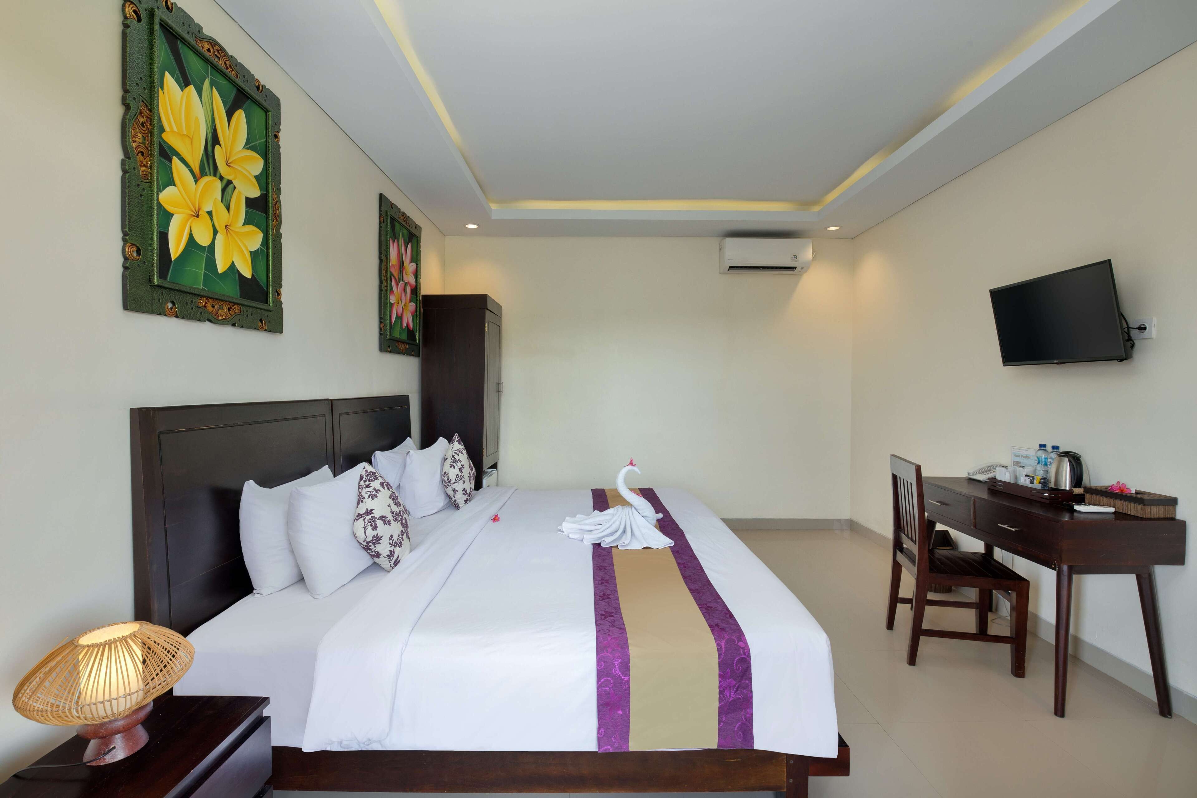 A hotel room with a bed, a desk, a chair, a TV, and artwork on the walls.