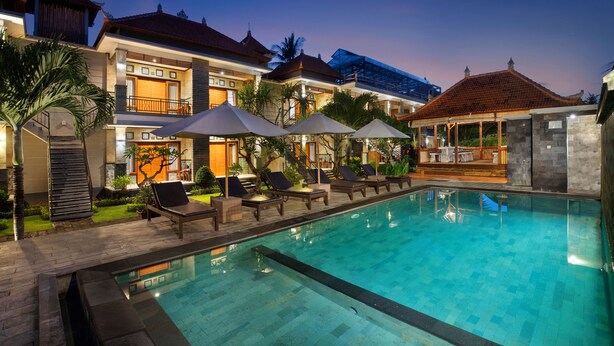 En swimmingpool med solstolar och parasoller, omgiven av byggnader med traditionell arkitektur.
