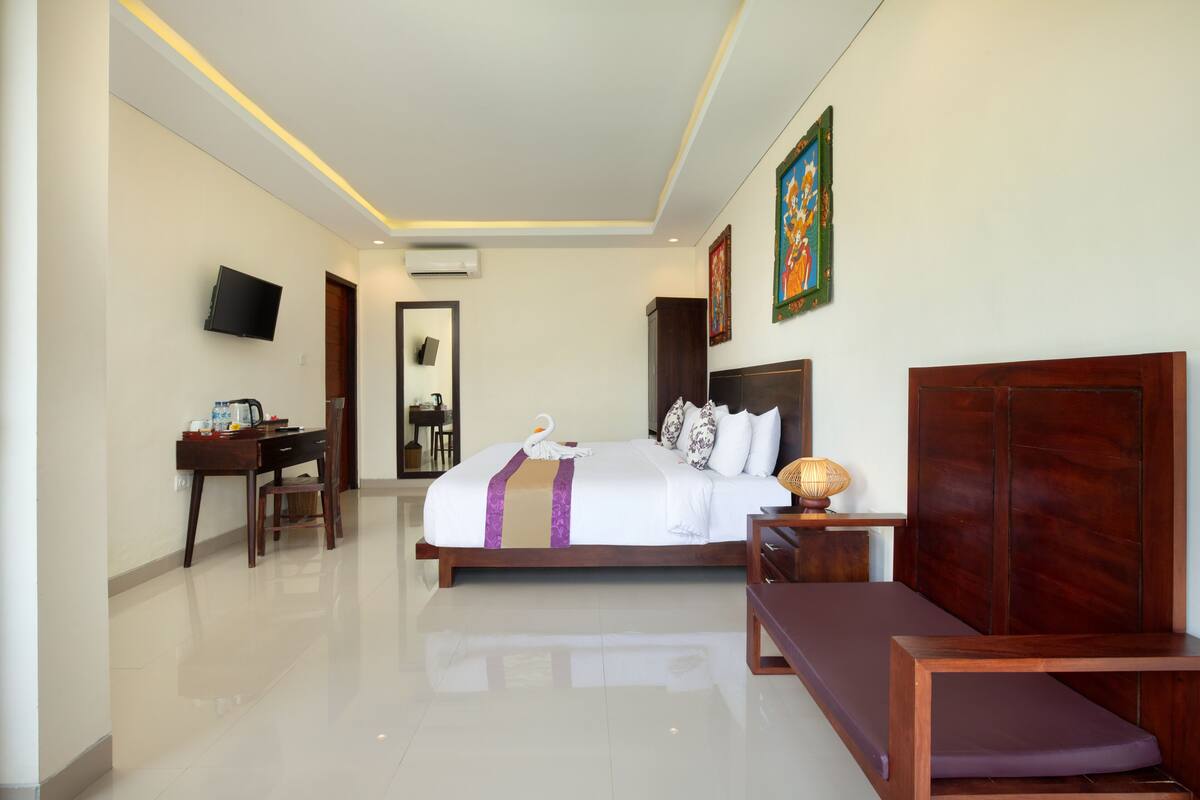 A hotel room with a bed, a desk, a TV, and a bench.