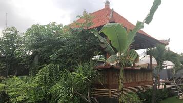 Un edificio tradicional con techo de tejas rojas, rodeado de abundante vegetación y una estructura de bambú.