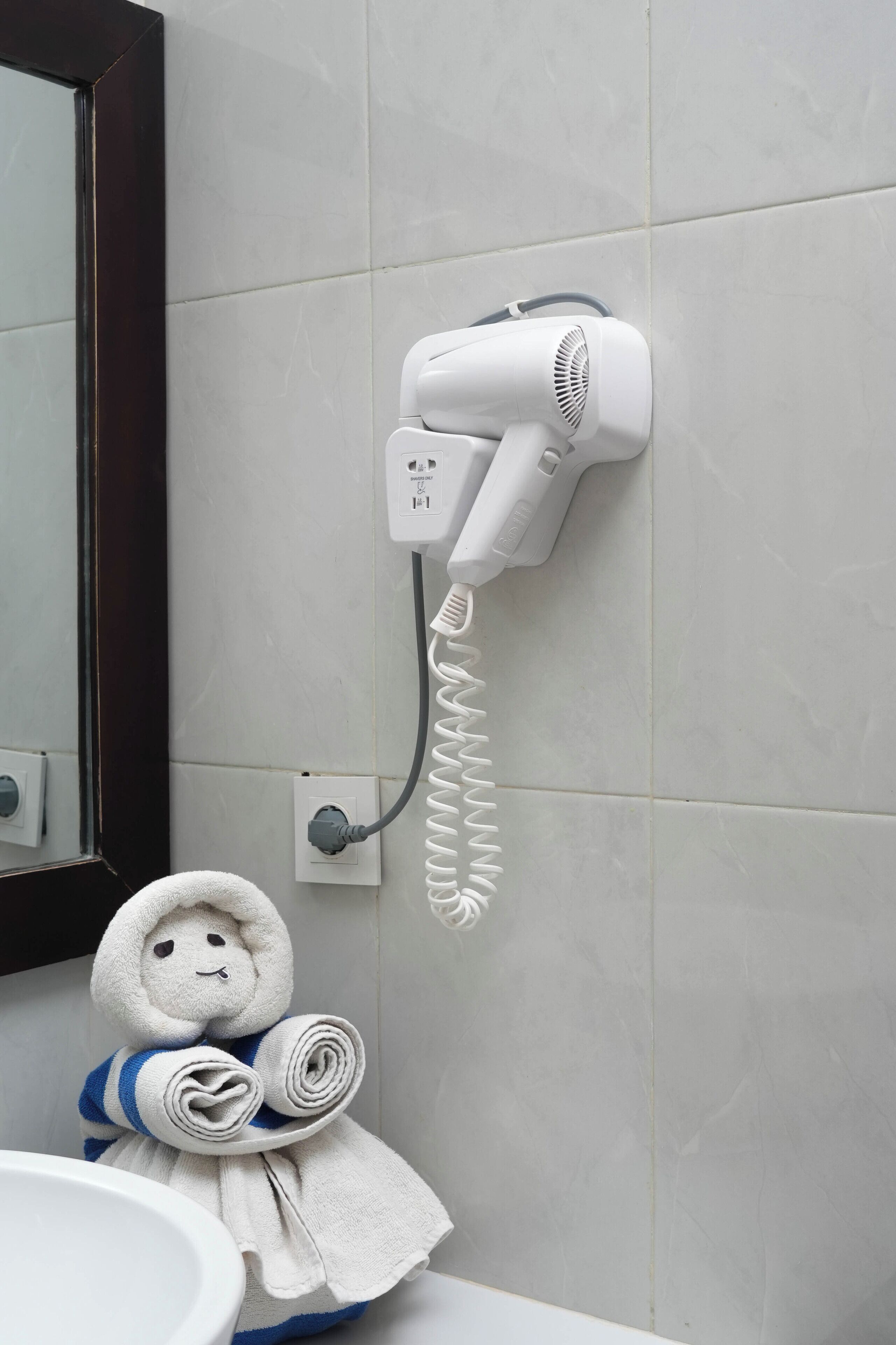 A bathroom with a hairdryer mounted on the wall, a towel rack, and a mirror.