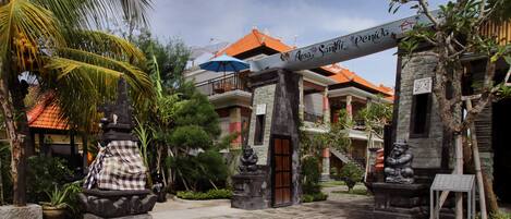 A traditional Balinese gate with a sign, palm trees, and a building with a tiled roof.