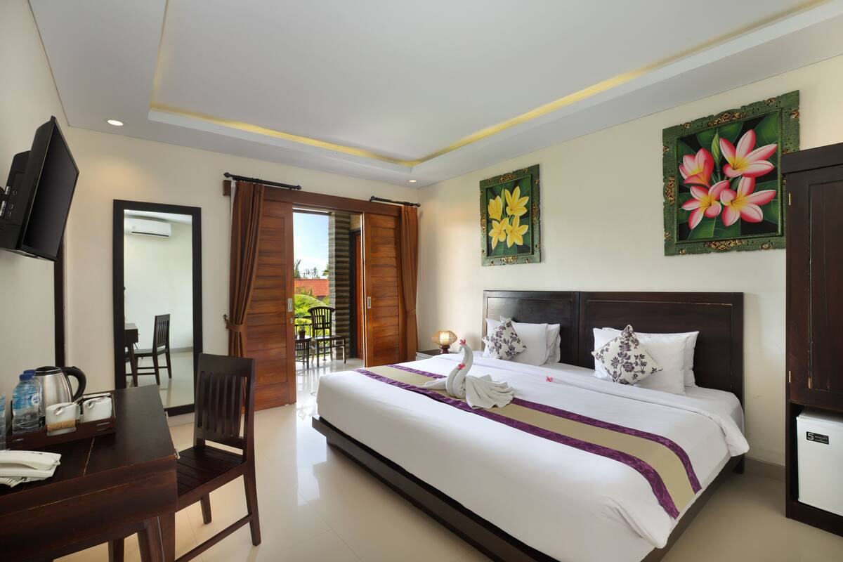 A hotel room with a bed, a desk, a chair, a television, and a balcony with a view of greenery.
