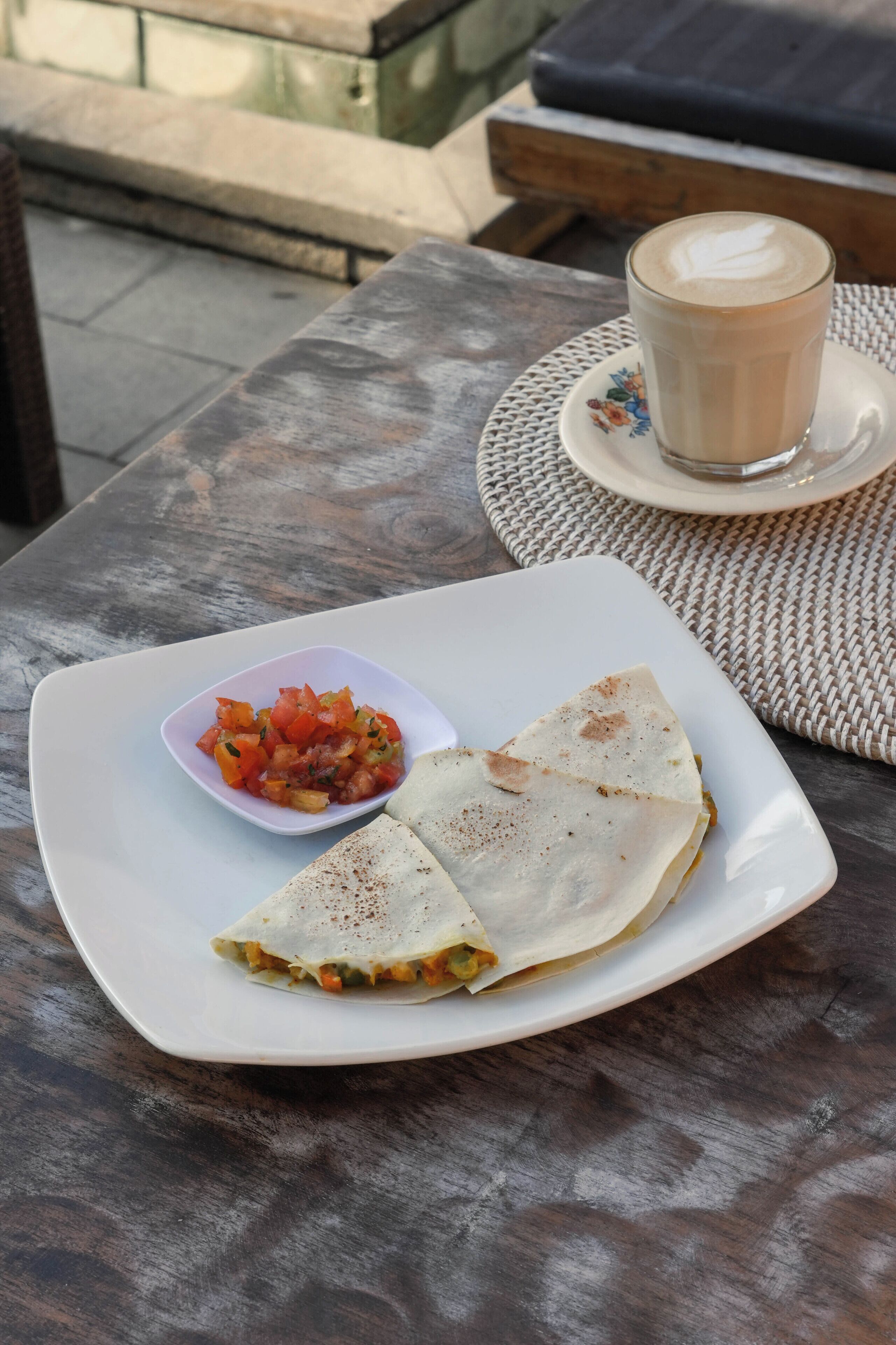 Een maaltijd bestaande uit een quesadilla, salsa en een kop koffie op een tafel.