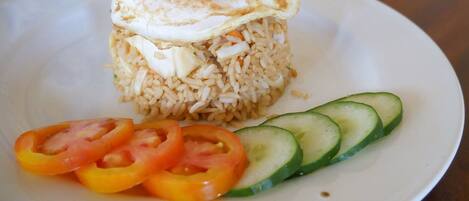 A plate with fried rice topped with a fried egg, accompanied by sliced tomatoes and cucumbers.