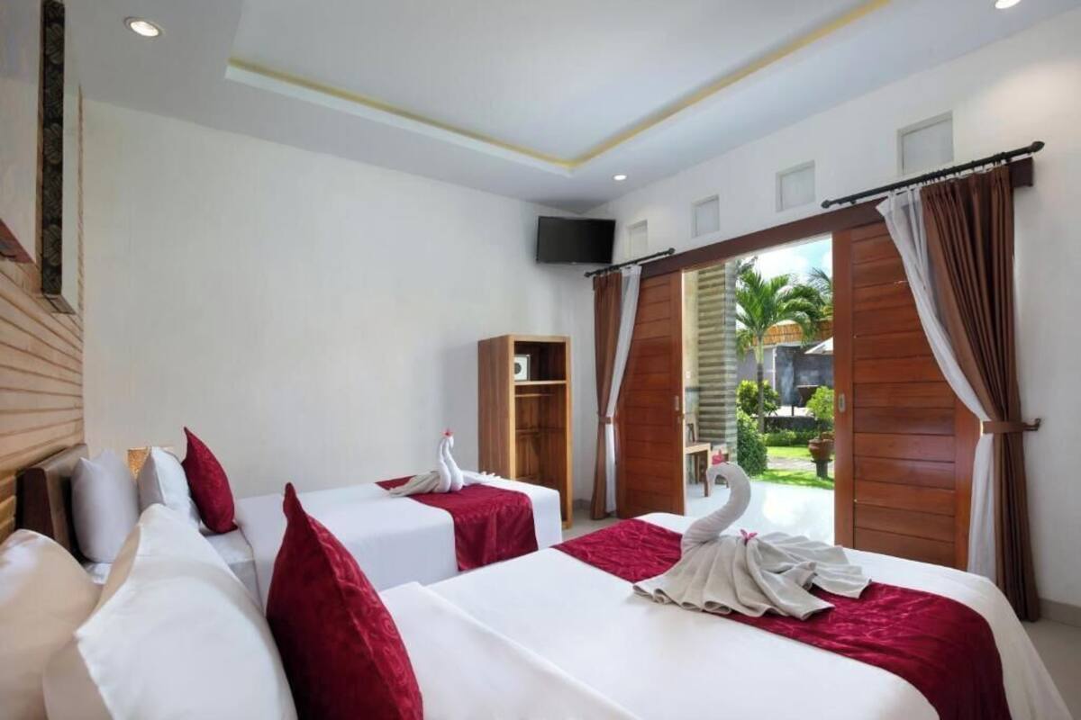 A hotel room with two beds, a wooden wardrobe, a TV, and a view of the outdoors.