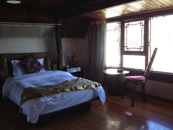 A bedroom with a bed, a chair, a small table, and a window with curtains.