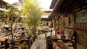 A traditional courtyard with stone pathways, wooden benches, and potted plants. - Lijiang Taohuadao Post Inn (Lijiang)