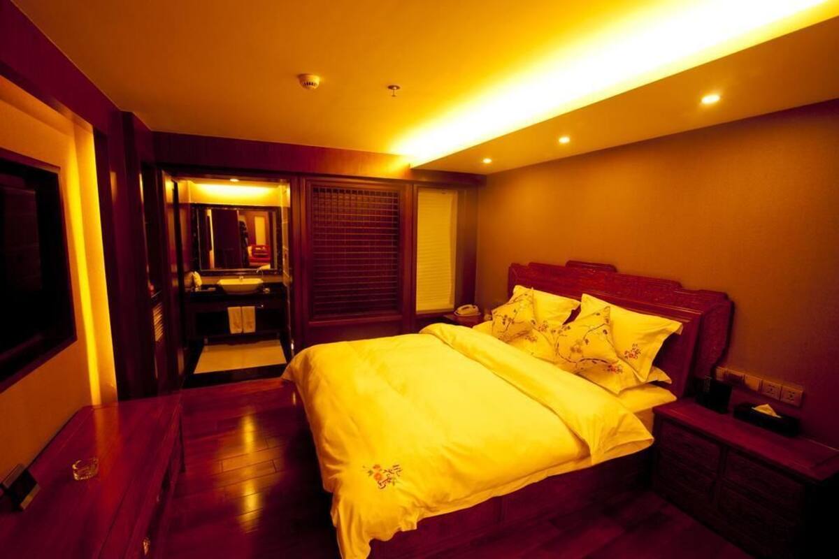 A bedroom with a large bed, wooden flooring, a nightstand, and a mirror.