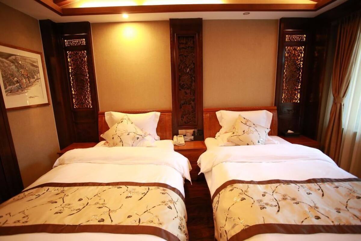 A hotel room with two beds, wooden headboards, a nightstand with a phone, and a framed picture on the wall.