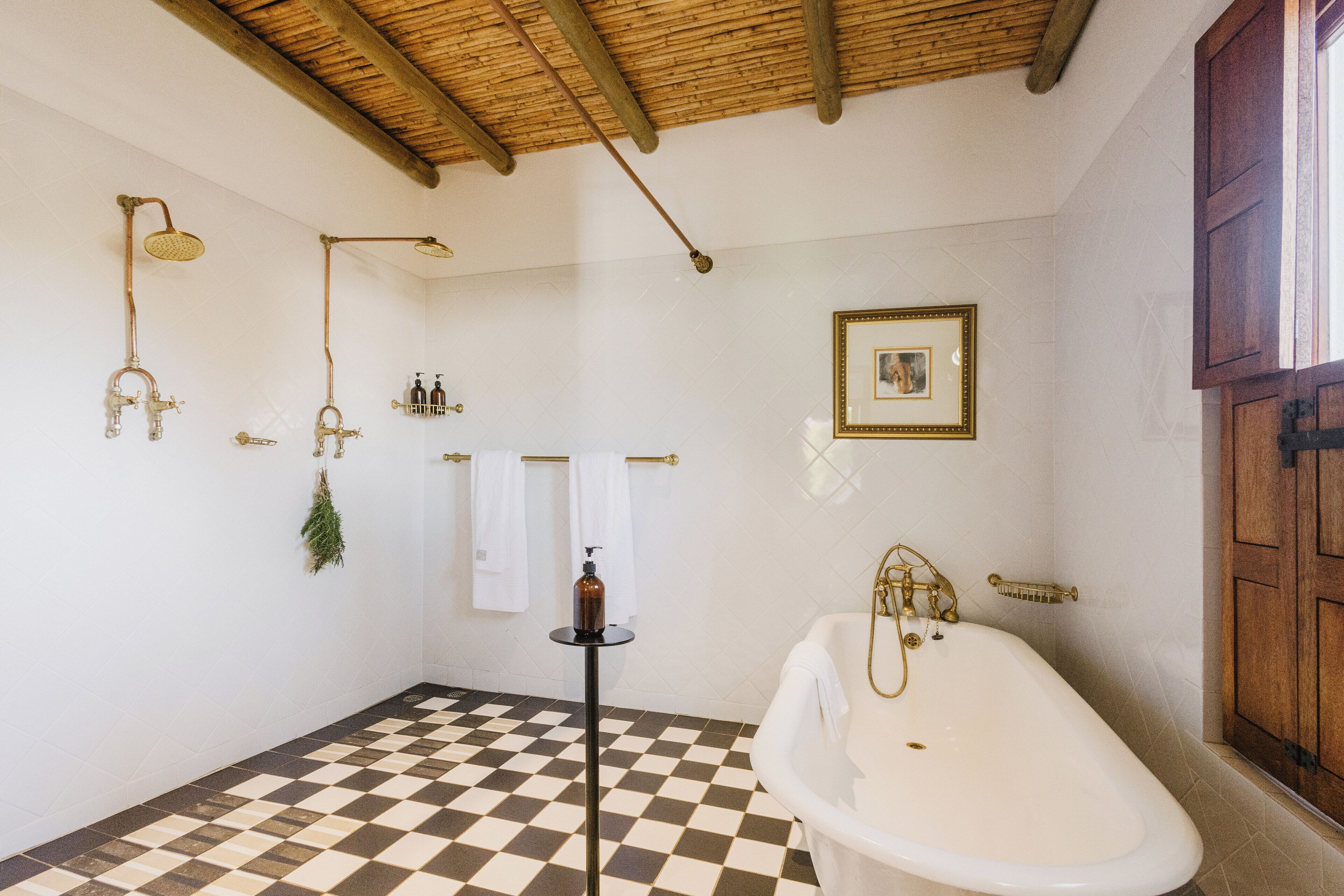 Un baño con piso a cuadros, una bañera, una ducha con grifo dorado y un cuadro en la pared.