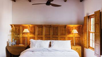 Un dormitorio con cabecera de madera, dos mesitas de noche con lámparas y un ventilador de techo.