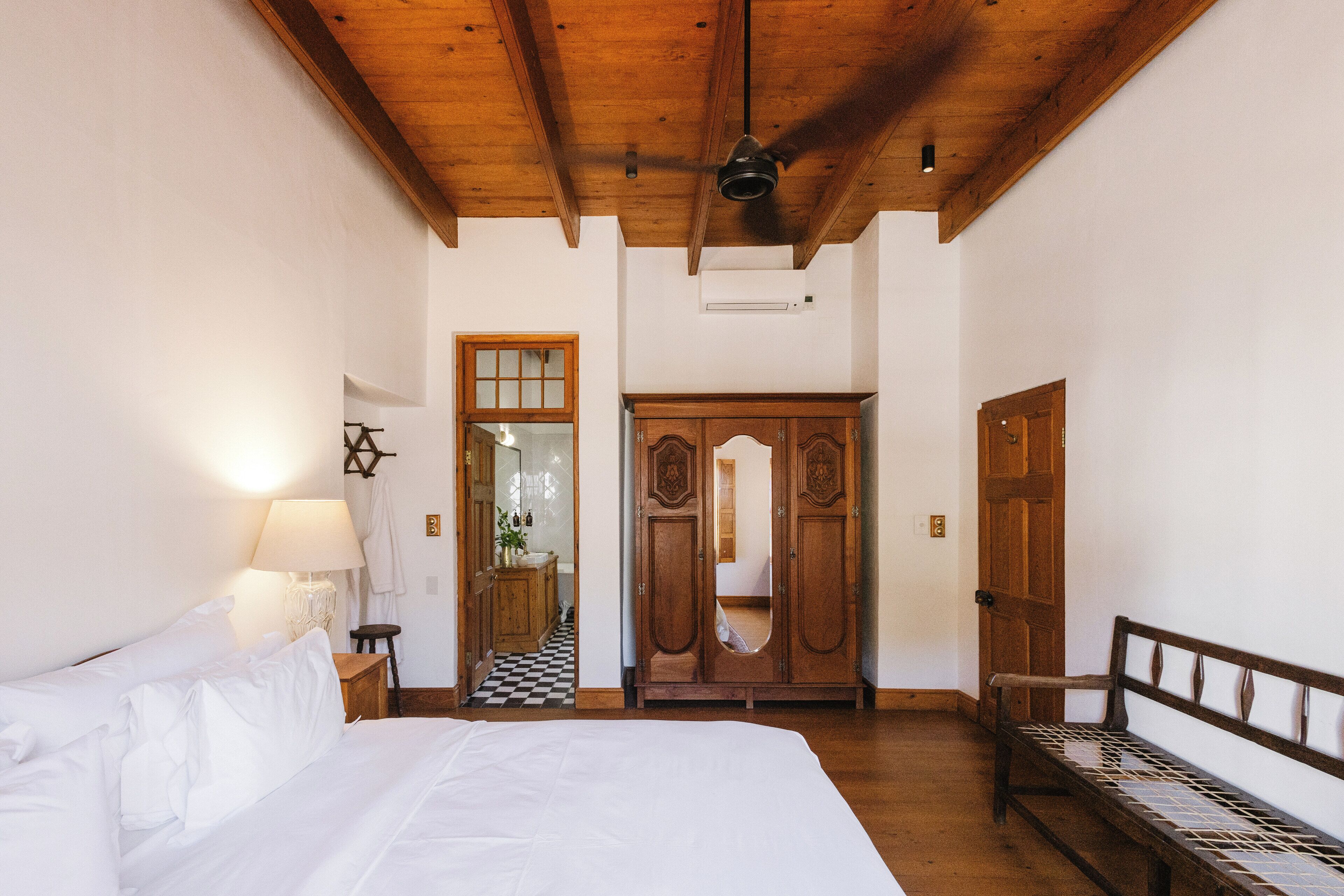 A bedroom with a bed, wooden wardrobe, and a bench.