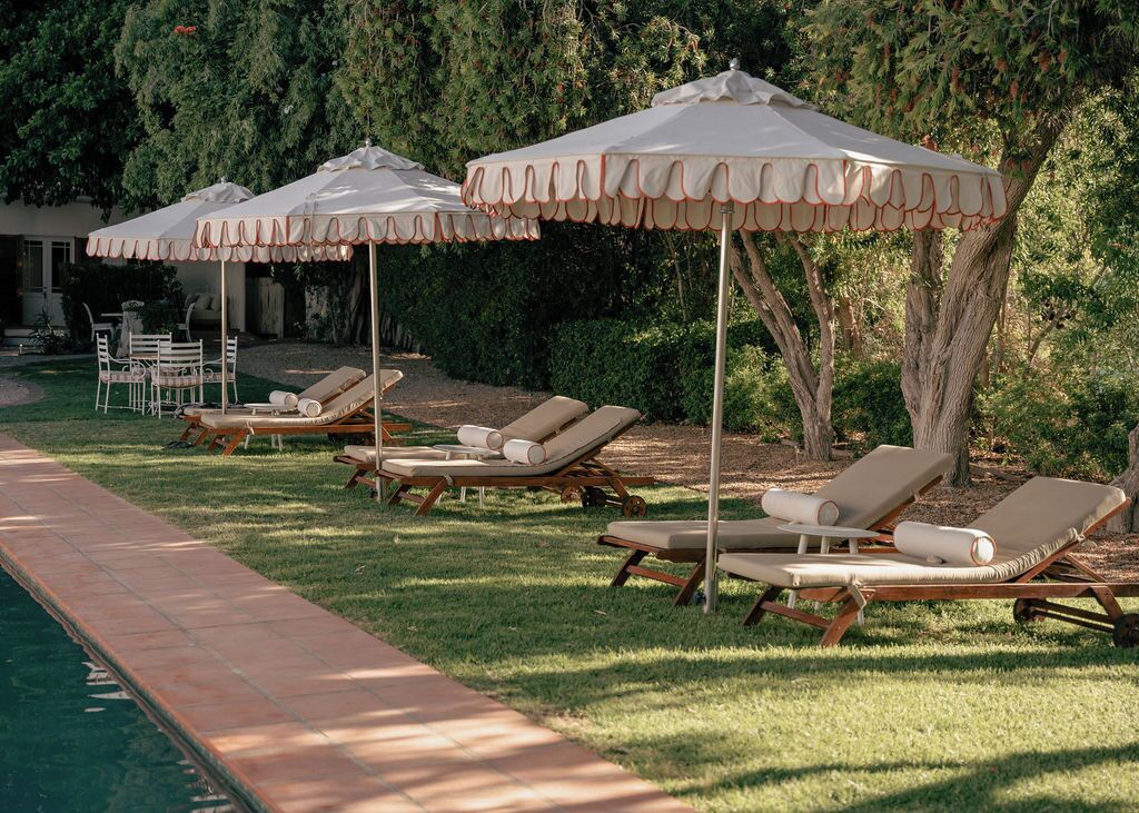 Een zwembadterras met ligstoelen en parasols, omringd door groen.