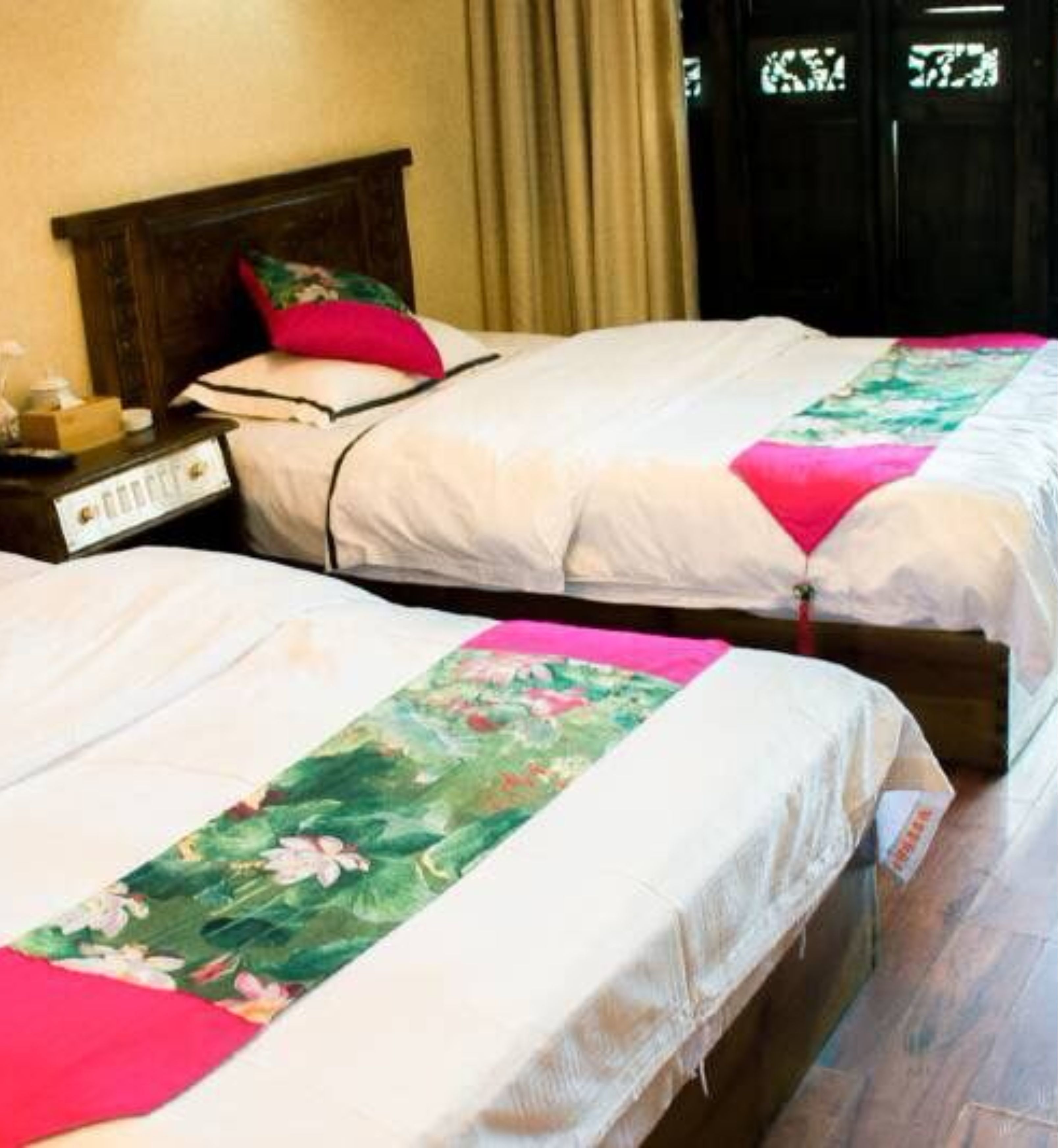 Dos camas individuales con cabeceros de madera, ropa de cama blanca y colchas estampadas con motivos florales.